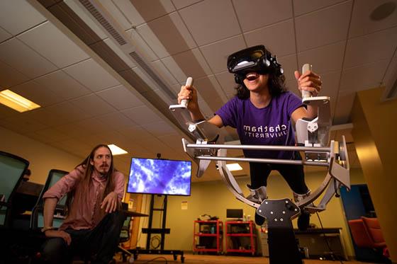 Photo of a Chatham University student in a virtual reality machine in the Immersive Media lab, while a professor watches